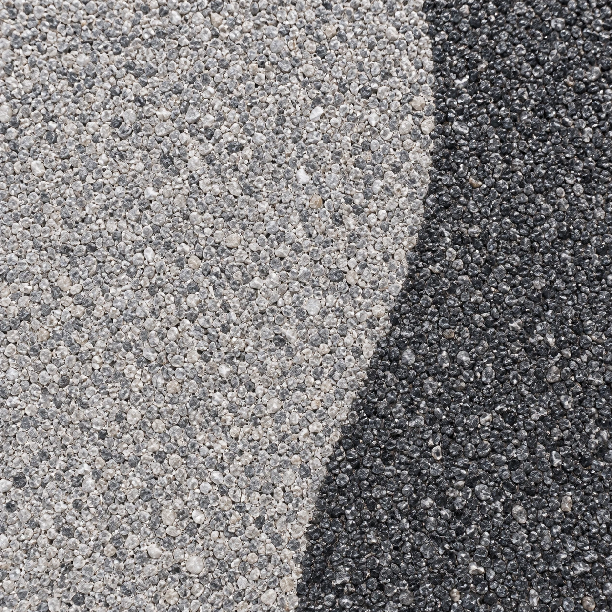Gros plan du granulat gris perle à la jonction de la bordure anthracite.