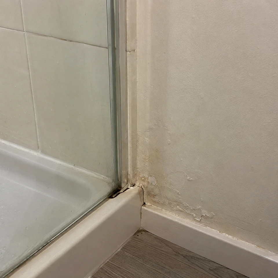 Traces et cloques sur le mur au bord d’une douche, près d’un raccord vieilli.