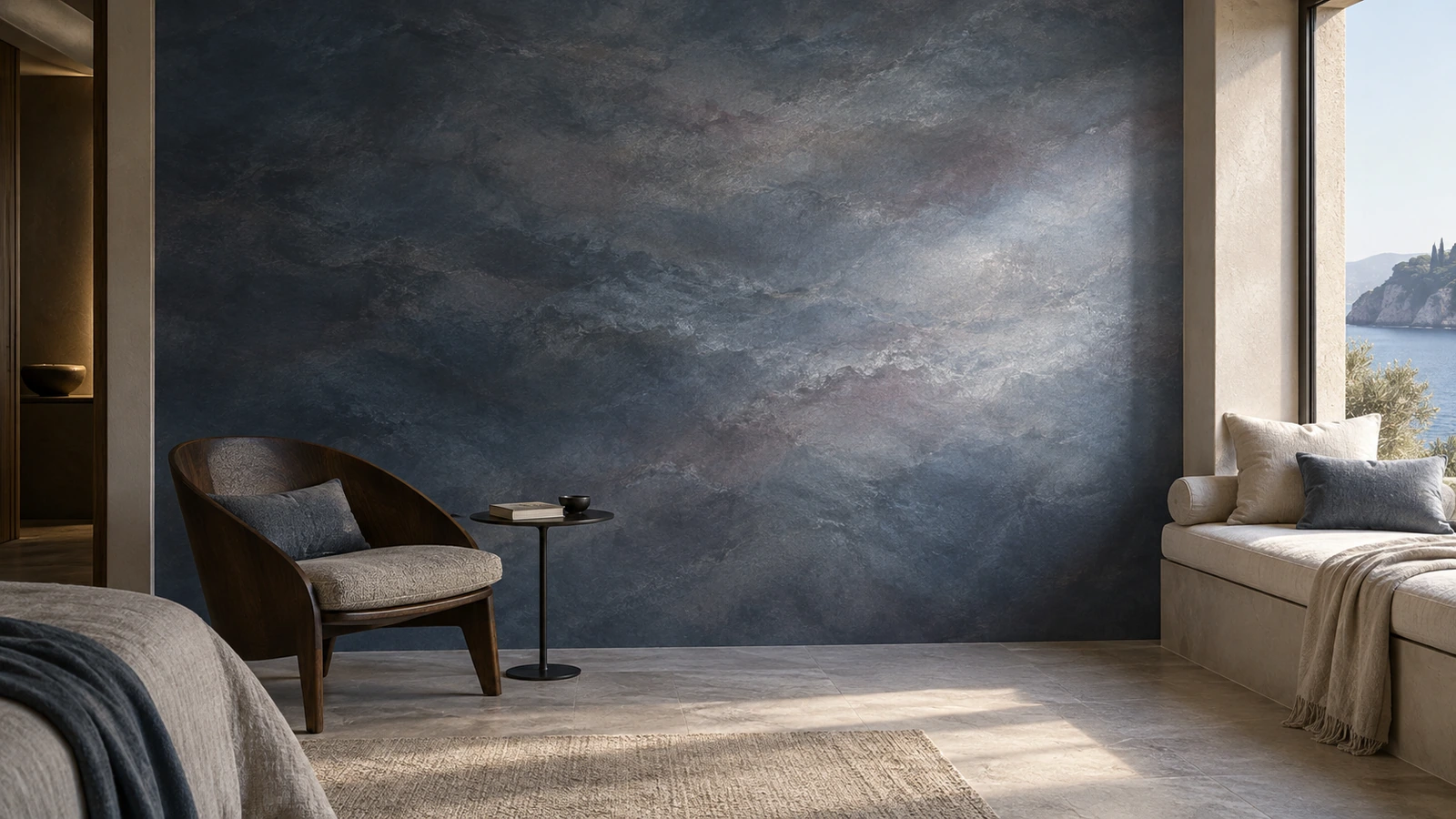 Chambre au mur bleu nuit en mouvement nacré, fauteuil sombre et banquette sous une fenêtre ouverte sur la mer