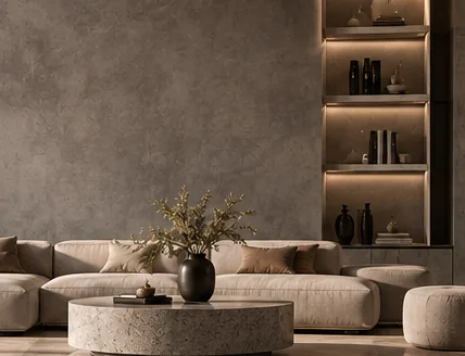 Salon au mur gris béton nuagé, canapé clair, table ronde minérale et étagères éclairées