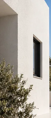 Mur de façade blanc et lisse percé d'une fenêtre sombre, sous un ciel bleu.