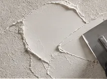 Mastic blanc étalé en voile fin sur un mur, bords de matière visibles.